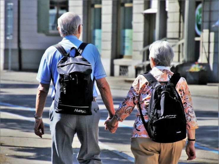 Old couple with backpacks holding hands