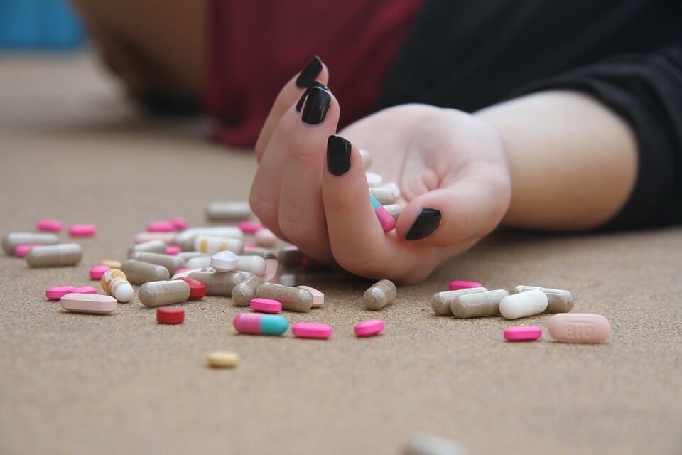 Teen girl's hand limp with pills spread around it