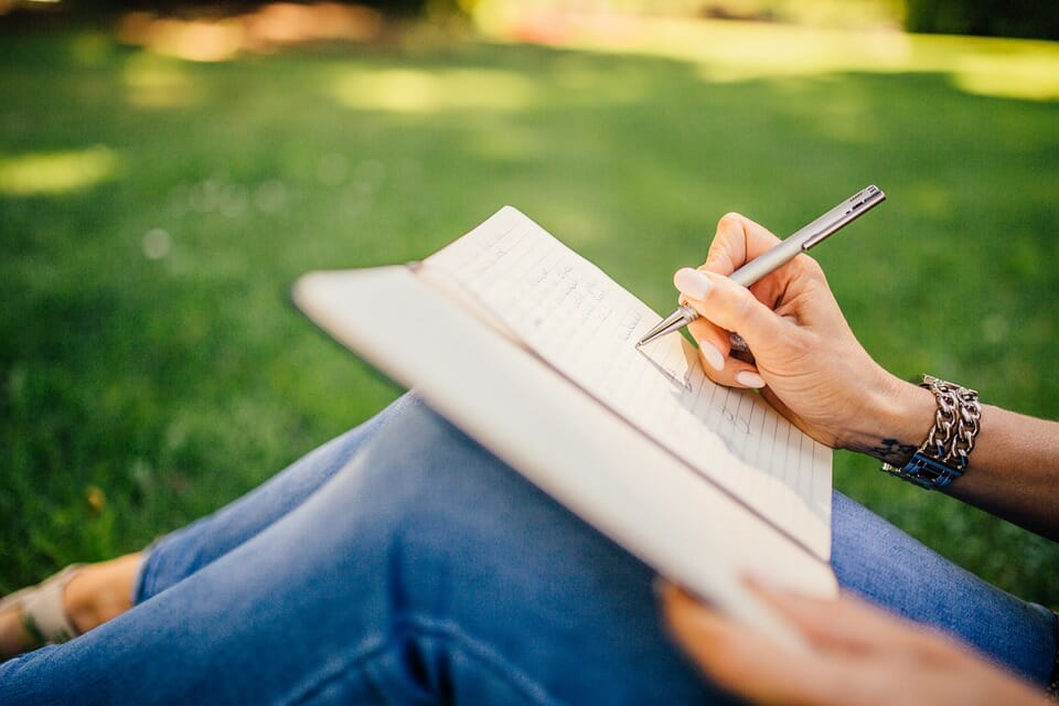 Woman writing in notebook on grass