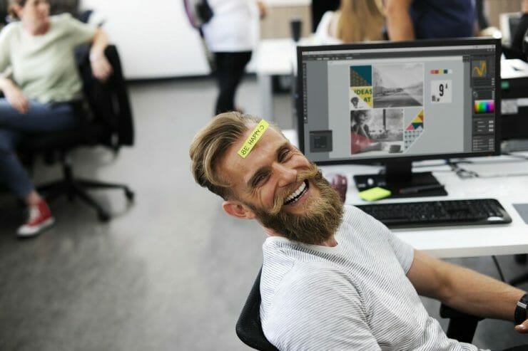 Man in office smiling with "Be Happy" sticker on his forehead