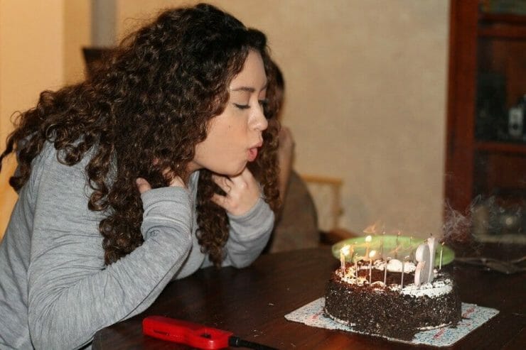 Teen girl blowing out candles on a cake at a birthday party