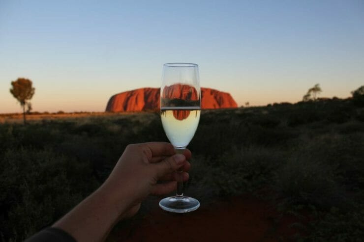 Hand raising wine glass to Ayre's Rock