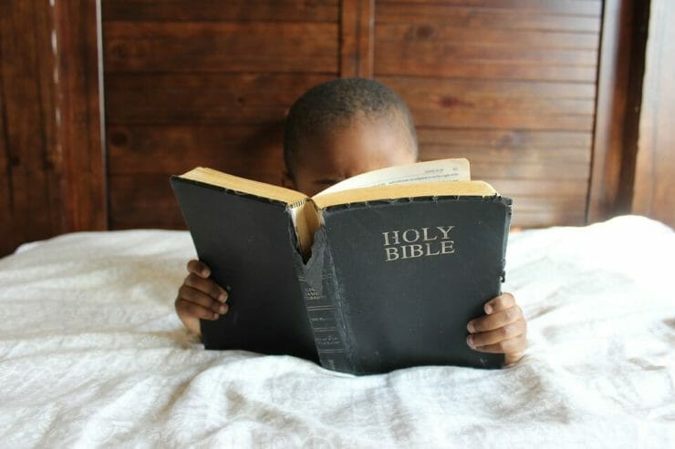 Black child reading the Bible in bed