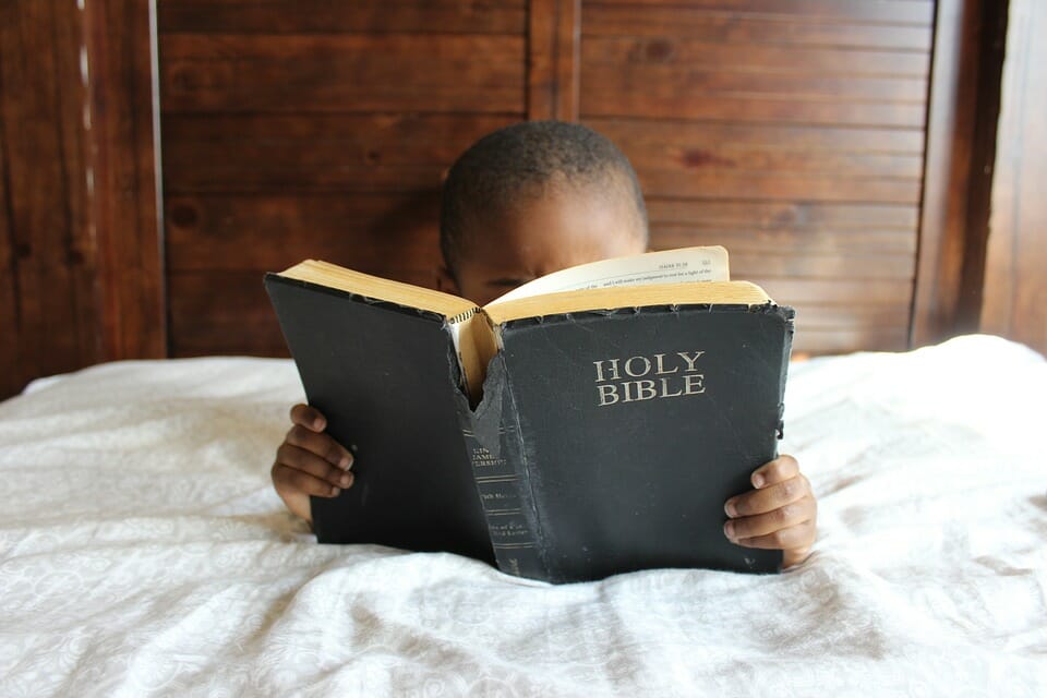 Black child reading the Bible in bed