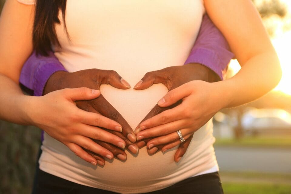 Love without boundaries - black man and pregnant white woman holding heart shaped hands