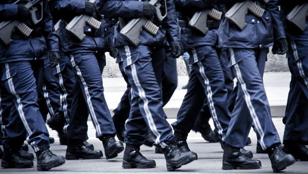 Soldiers marching in blue uniforms holding automatic rifles