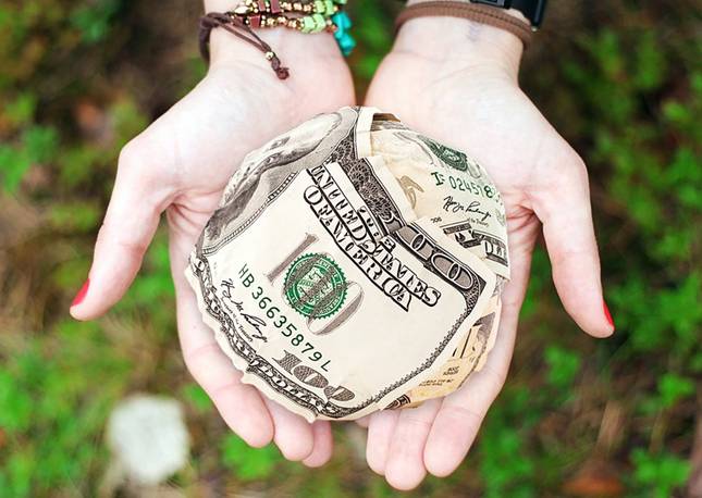 Hands holding a ball of $100 dollar bills