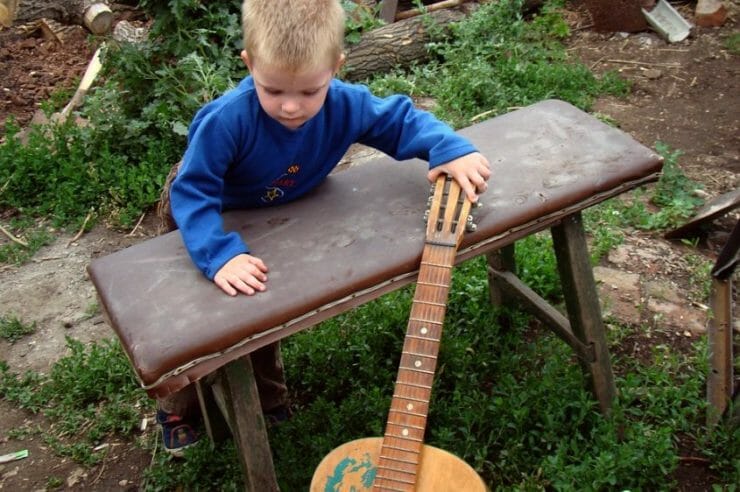 Little boy playing with a guitar in the back yard