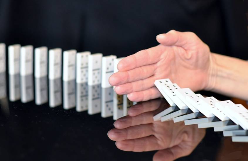 A row of dominos with a hand in the middle stopping them from continuing to fall