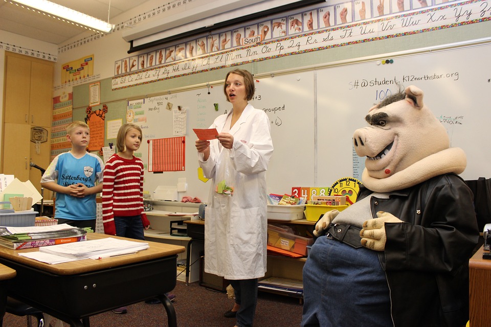 Teacher in a white coat and a pig sculpture with 2 children in a classroom