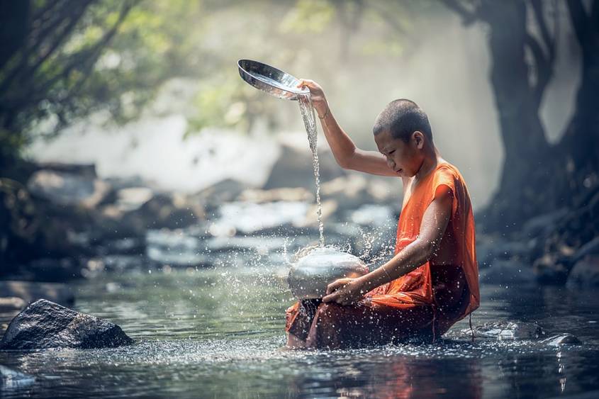 Buddhist monk child pouring water in a stream