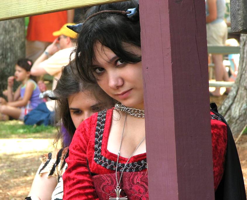Teenage girl in devil costume peeking shyly behind a post