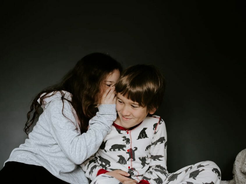 Girl in pajamas whispering to a boy in pajamas