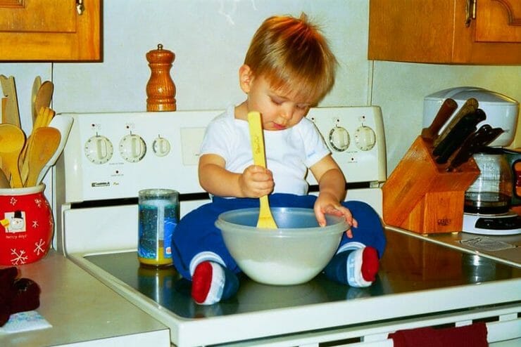 Little boy sitting on a stove stirring with a big spoon