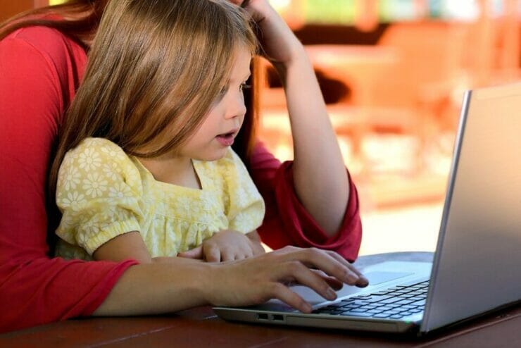 Little girl in her mother's lap in front of a laptop