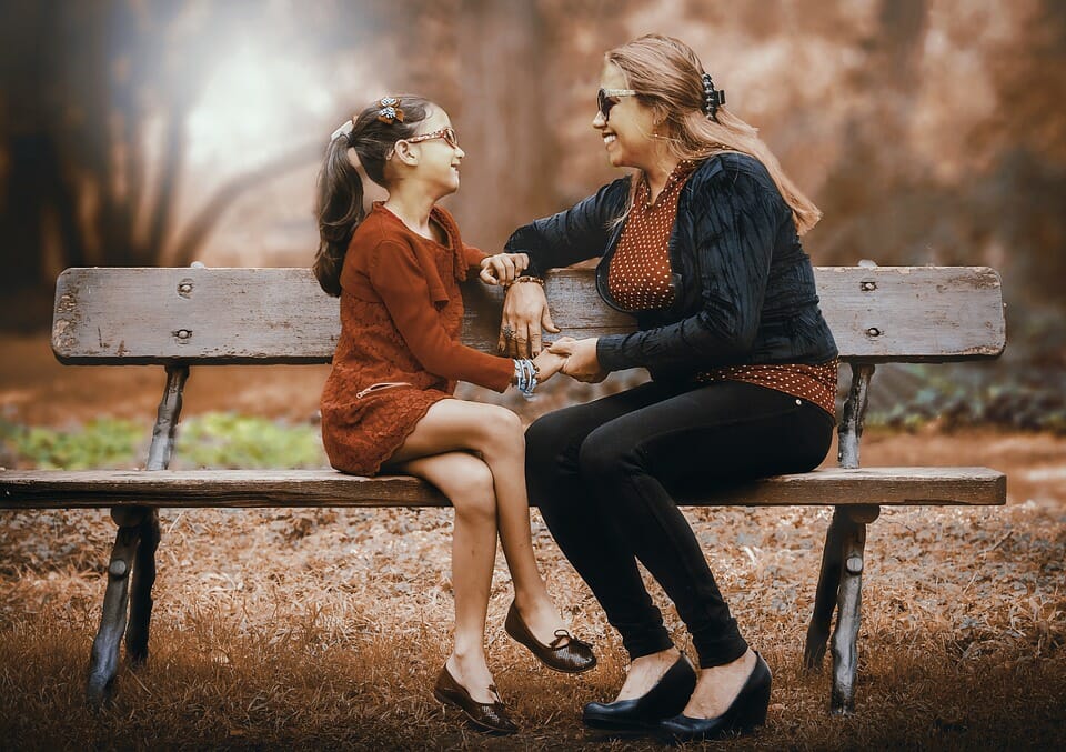 Woman and girl sitting on a park bench and smiling at each other