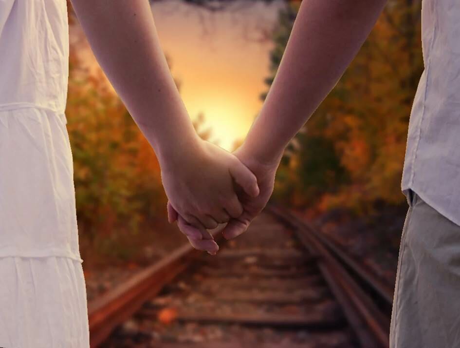 Man and woman holding hands on train tracks