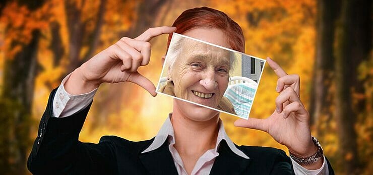 Young woman holding a photo of an old woman in front of her face - a lifetime perspective