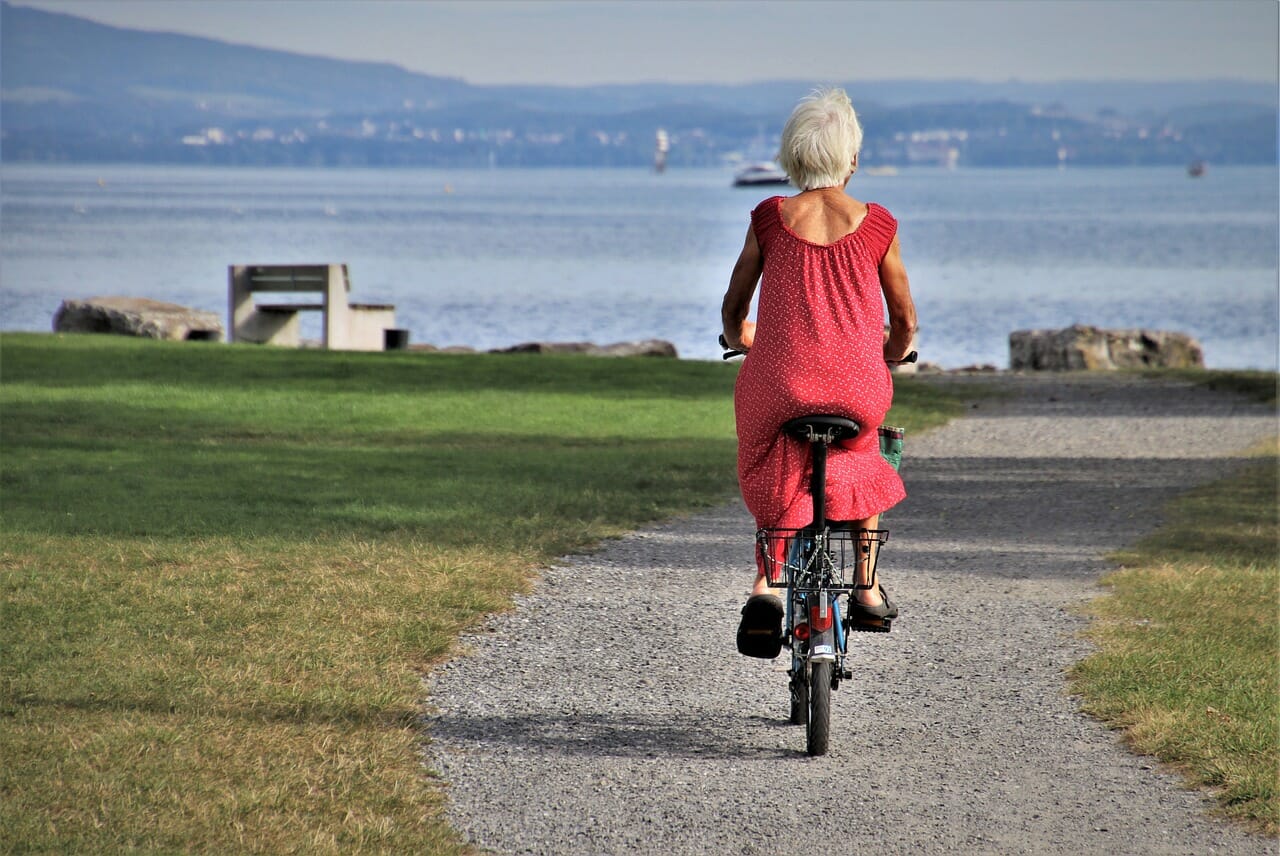 Old woman riding a bike towards a bay