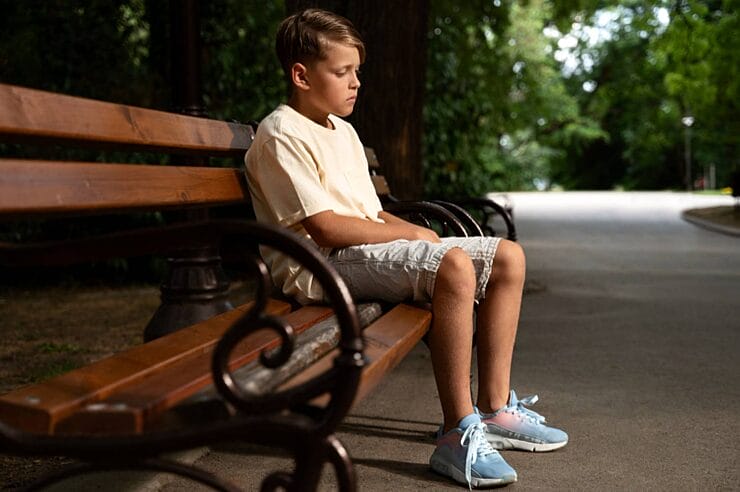 anti-social child sitting alone at playground watching other children play